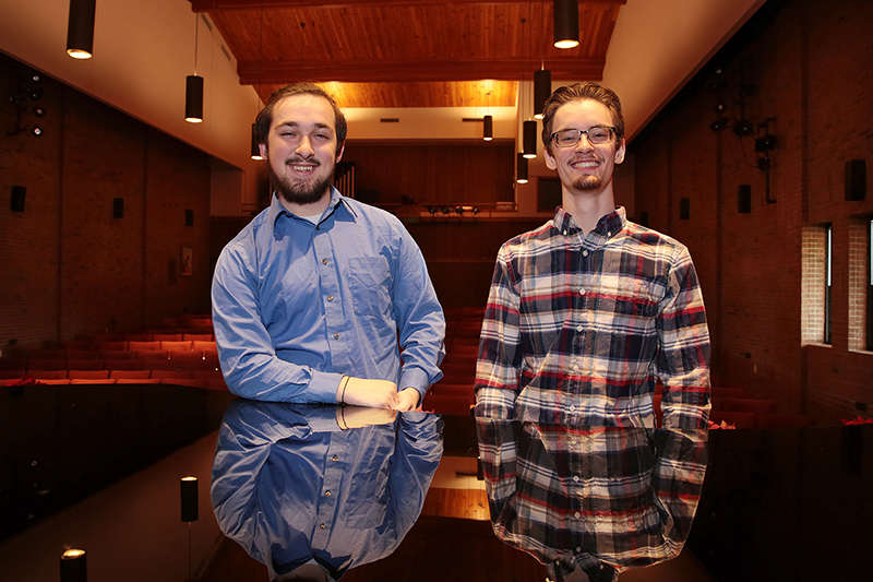 two male music students standing by piano