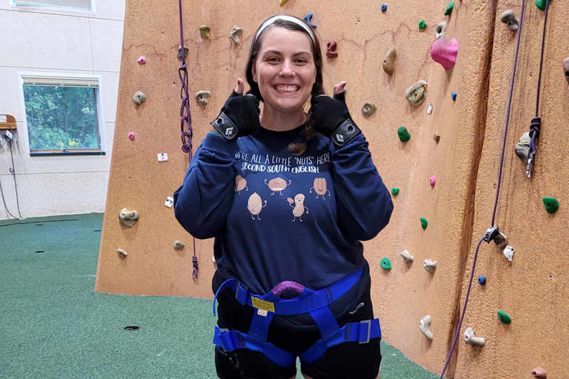 Rachel Weikert wearing rock climbing gear in front of climbing wall