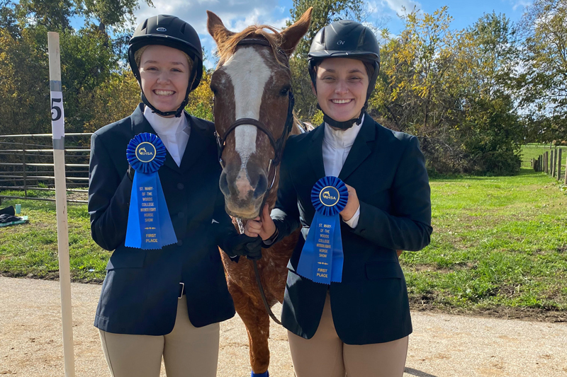two female students posing with horse and blue ribbons