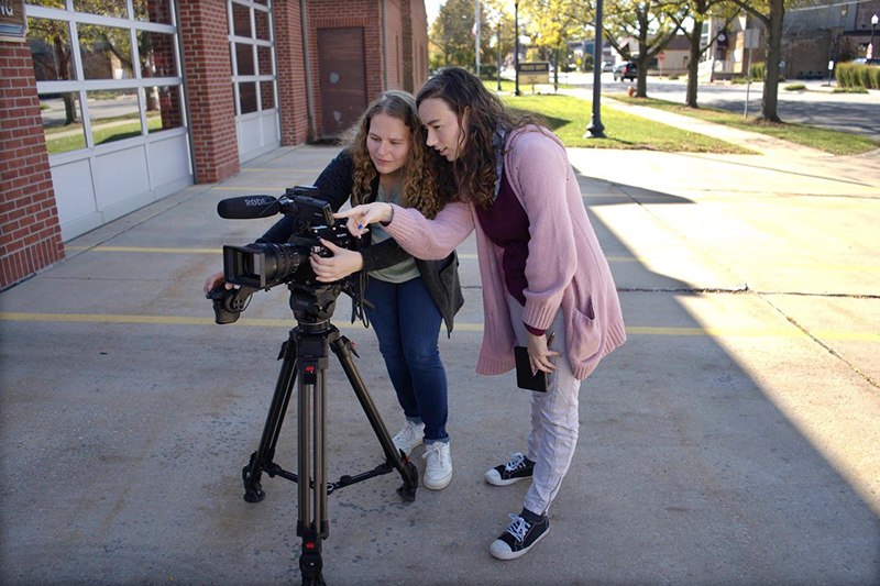 two film students work with a camera on a tripod outside