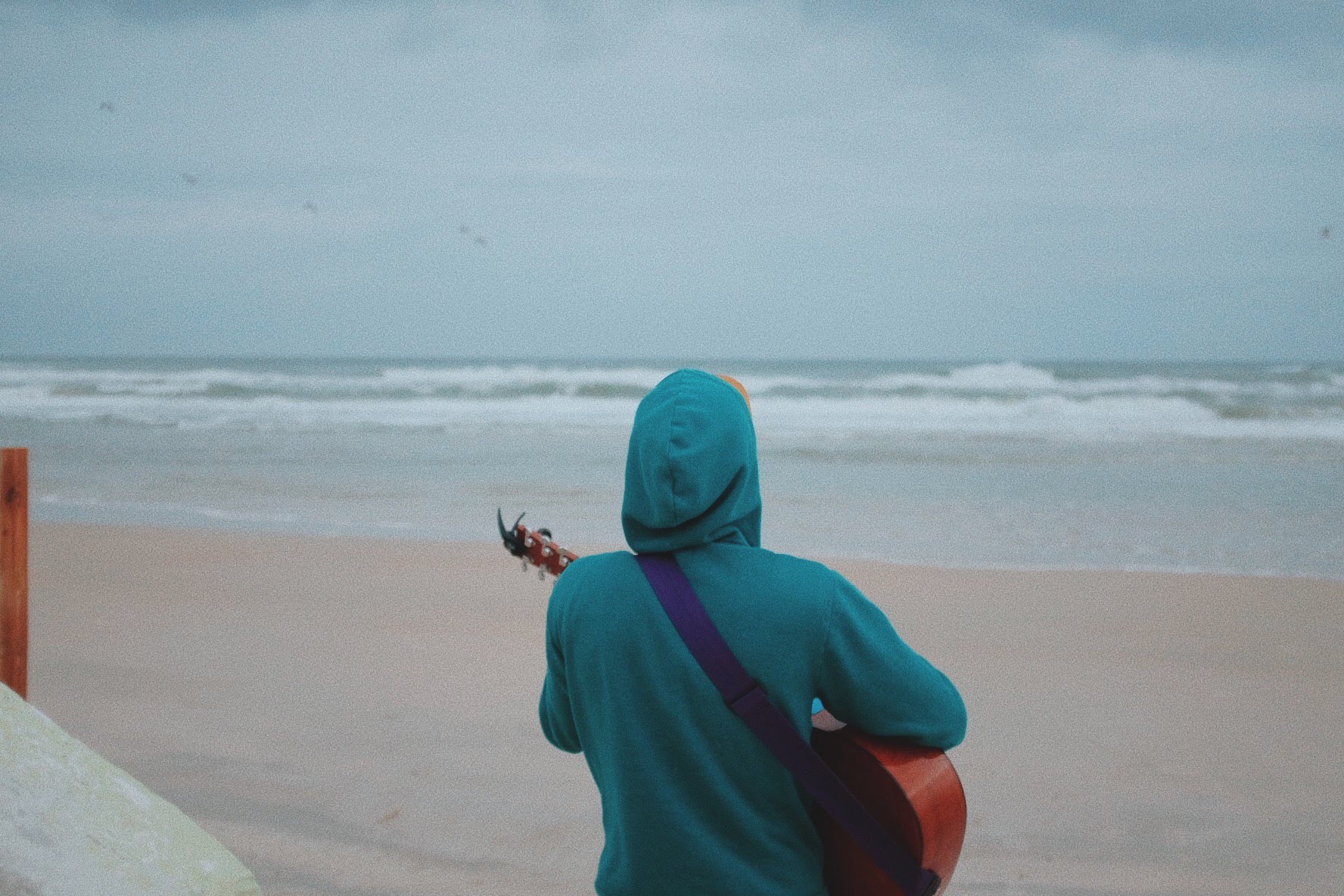 A hooded student playing guitar on the beach