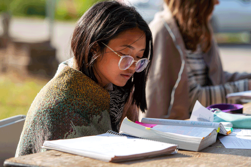 A student with glasses reading outside