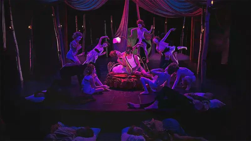 A couple on a bed with dancers surrounding them in A Midsummer Night’s Dream