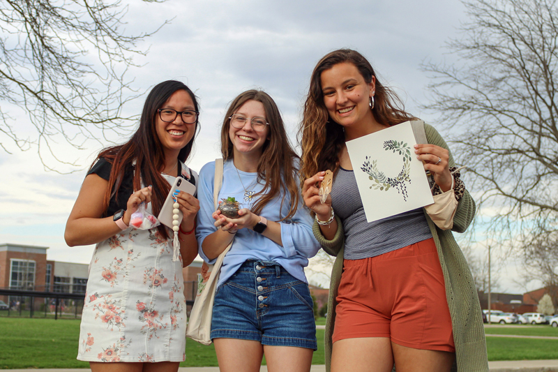 Three female students holding purchased items from Shop the Loop