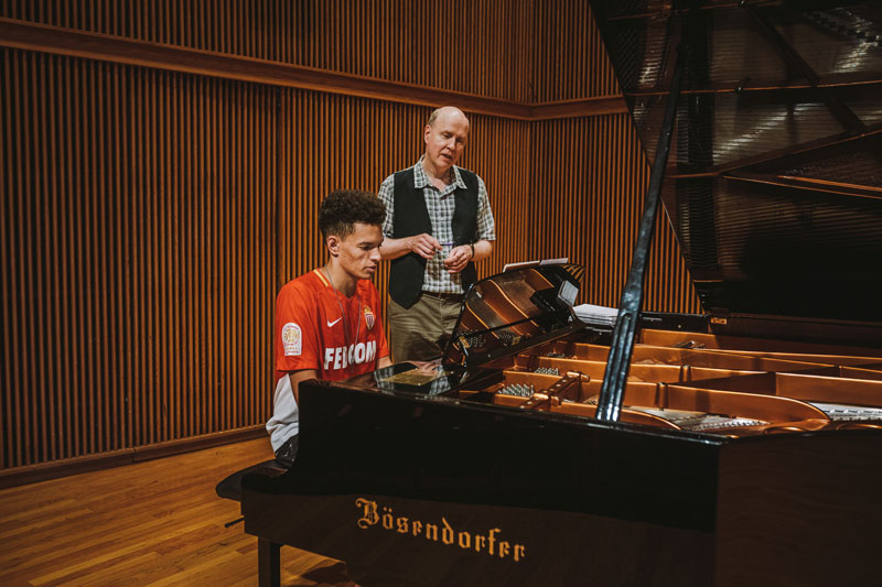 Professor teaching a student playing the grand piano