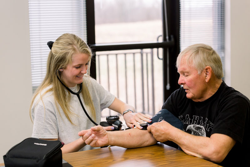 A student taking an older man's blood pressure