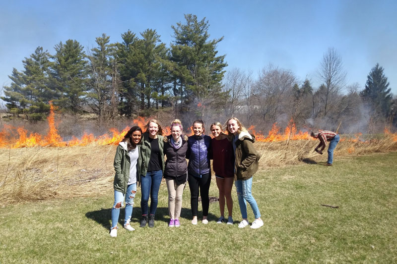 A group of female students standing in front of a prairie burning