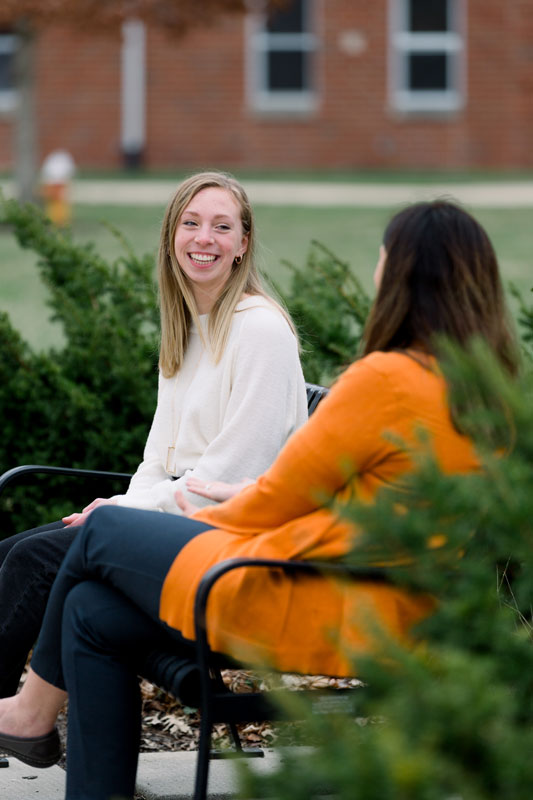 Two students talking on a bench outside Samuel Morris Hall