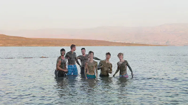 Six male students covered in mud standing waist deep in water