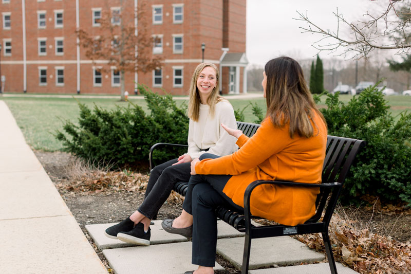 Two students conversing on a bench outside Samuel Morris Hall