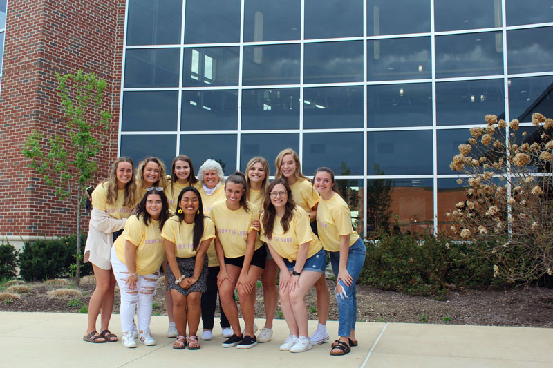 A group of students posing with a professor all in yellow shirts