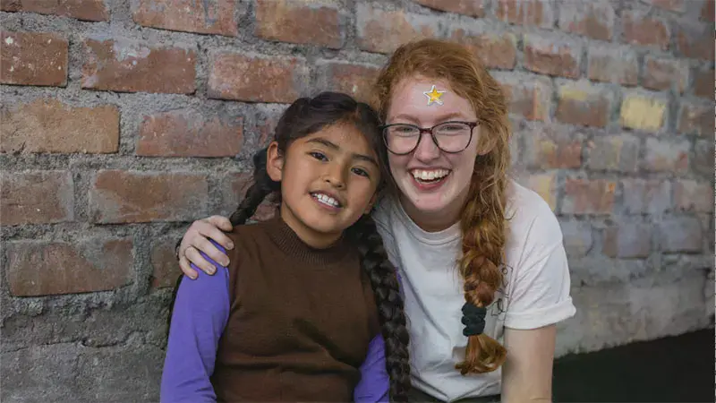 Taylor student with a sticker on her face embracing a young girl