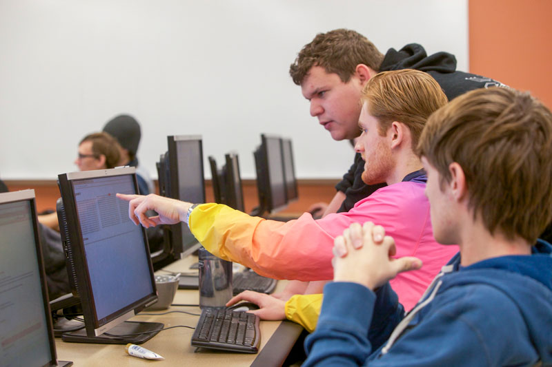 Student pointing at monitor as others look intently