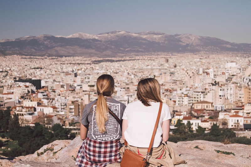 Two students sitting and overlooking a Greek city
