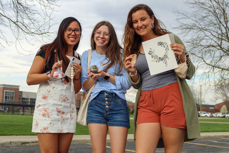 Three female students holding products from Shop the Loop