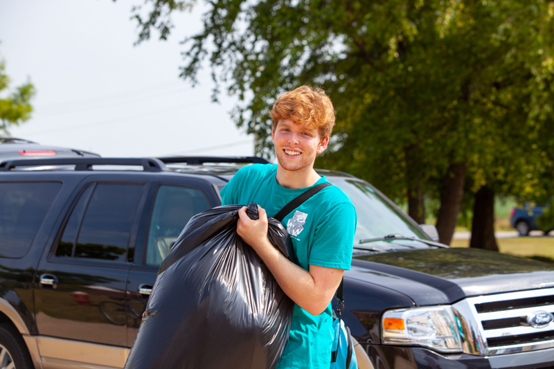 A student in a teal shirt helping freshmen move in