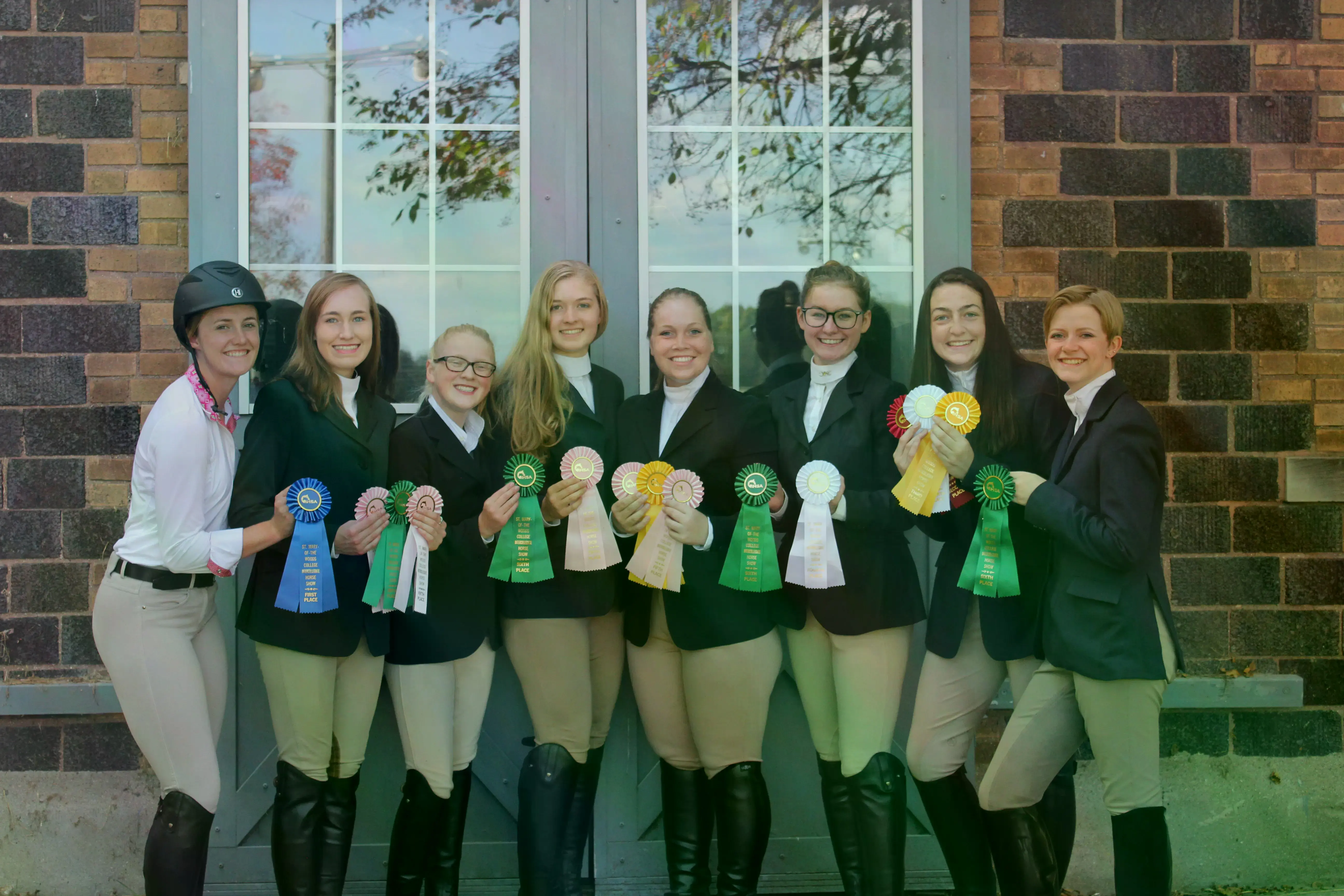 The equestrian team in front of a brick wall holding their ribbons