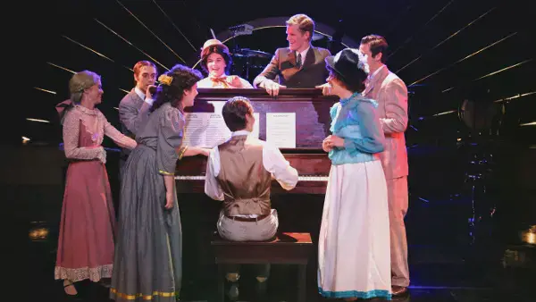 A group crowded around a man playing piano in I Love a Piano