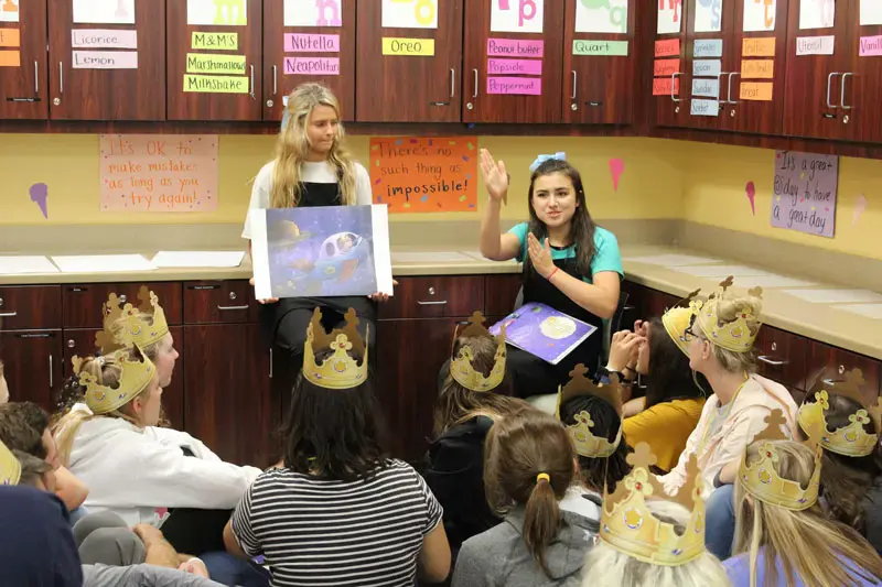 Two female students reading a storybook to a classroom