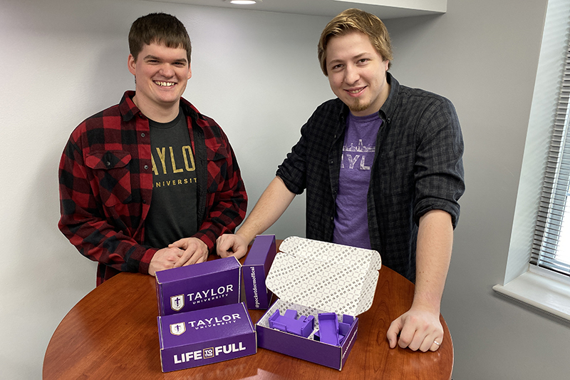 two male students stand behind box sets of Pocket Dorm