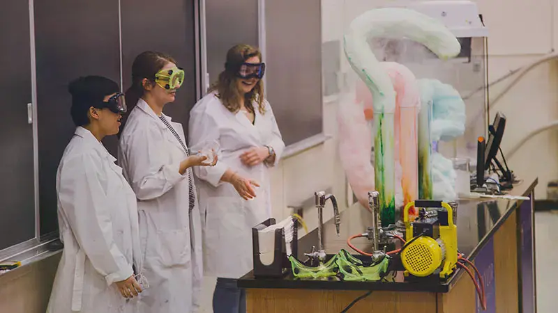 Three female Chemistry students watching a colorful chemical reaction