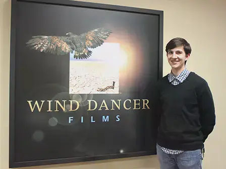 Student standing in front of a movie poster for Wind Dancer Films