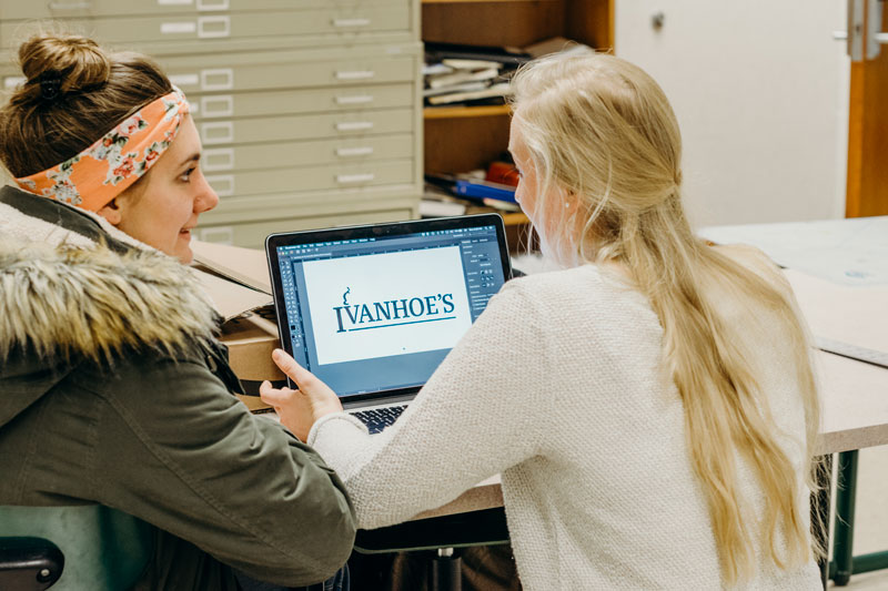 Two students taking while working on a redesigned logo for Ivanhoe's
