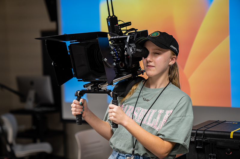 student using a camera on her shoulder