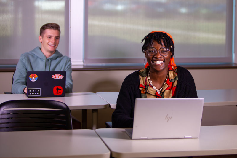 Two students smiling no their laptops in class