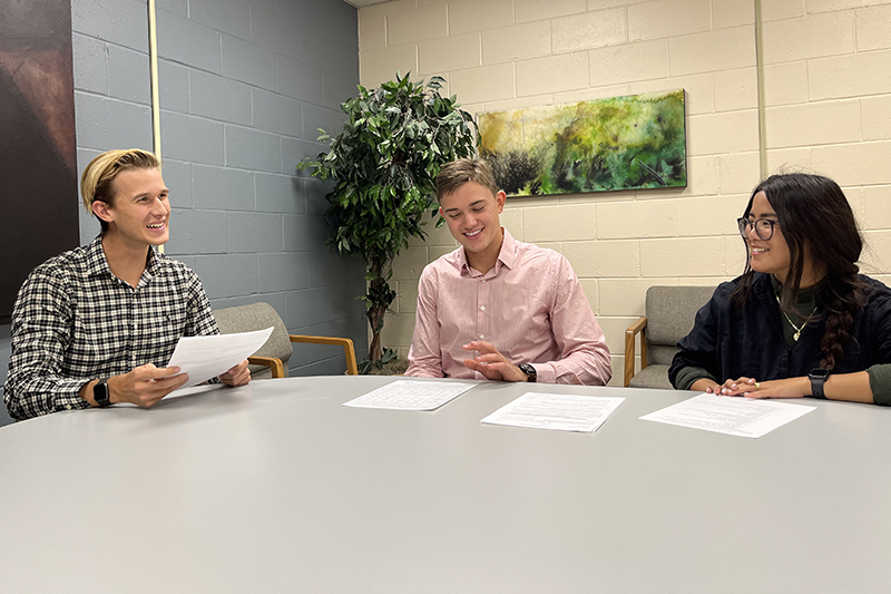 three students sit at table with paperwork