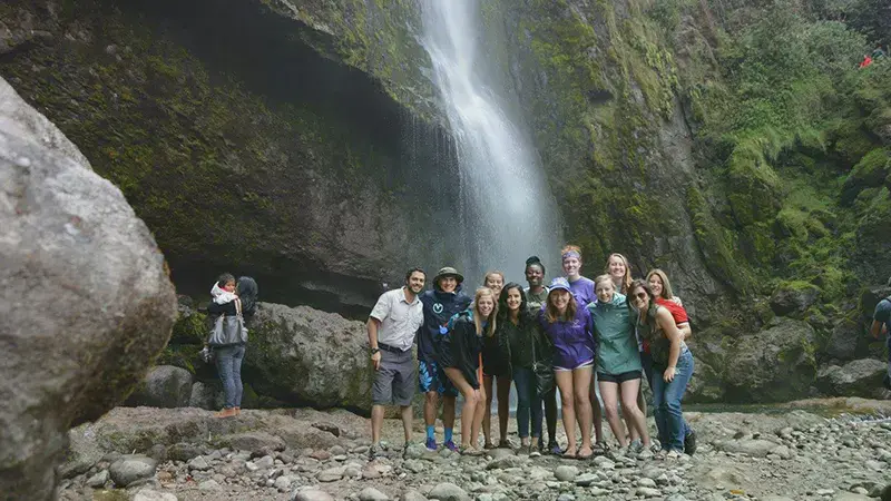 Group of students standing in front of a forest waterfall