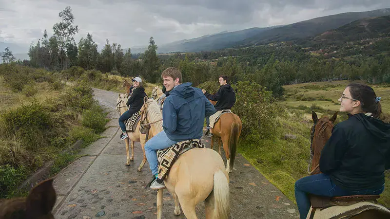 A group of Taylor students riding horses down a cobblestone road