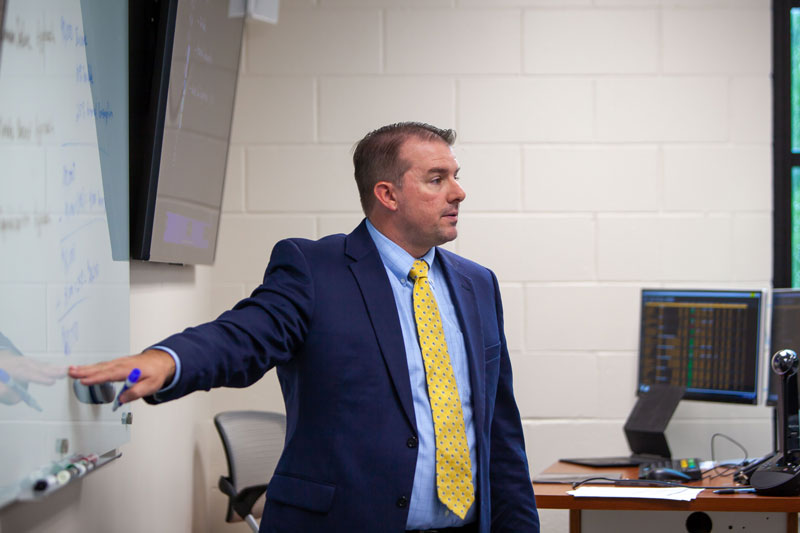 Taylor professor pointing at whiteboard while teaching class