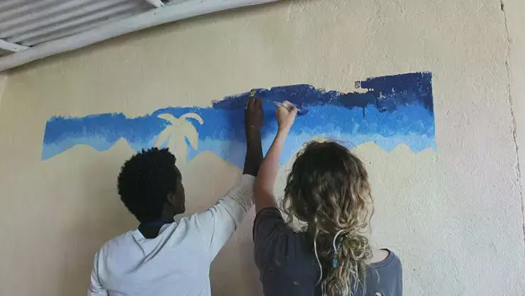 A couple of students painting a blue sky on a wall