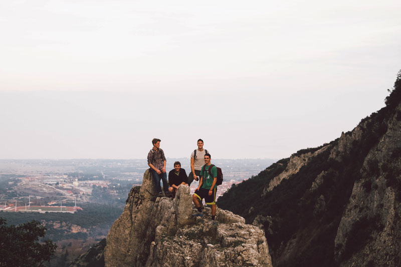 A few students standing atop a rock on a mountainside