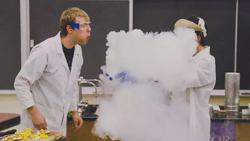 Taylor student blowing on a container of dry ice letting off smoke