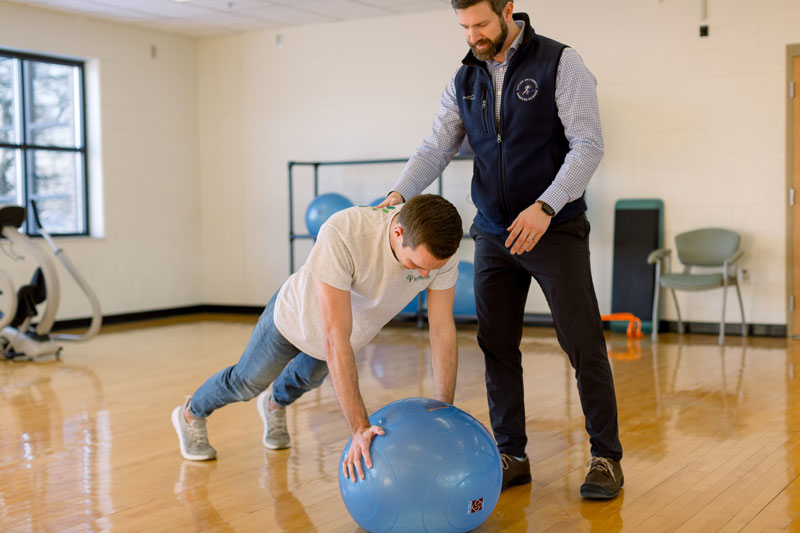 A professor stabilizing a student doing push ups on an exercise ball