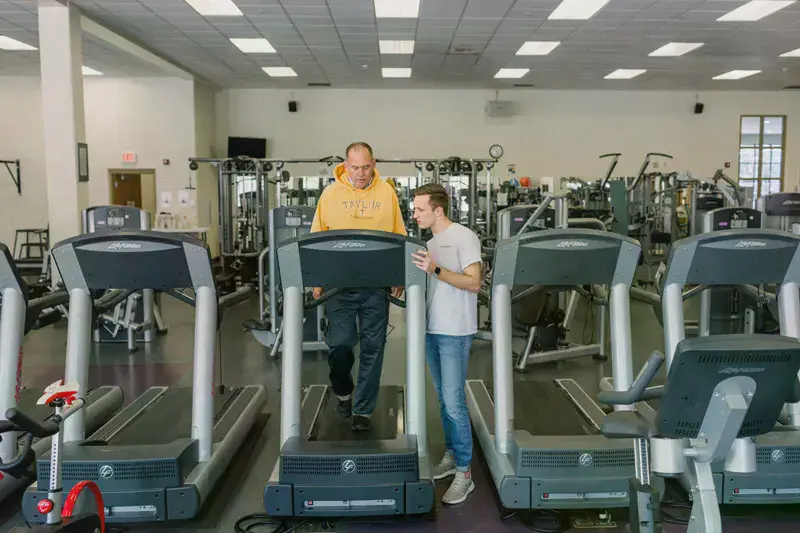 Student helping a man use a treadmill with the Invitation Program