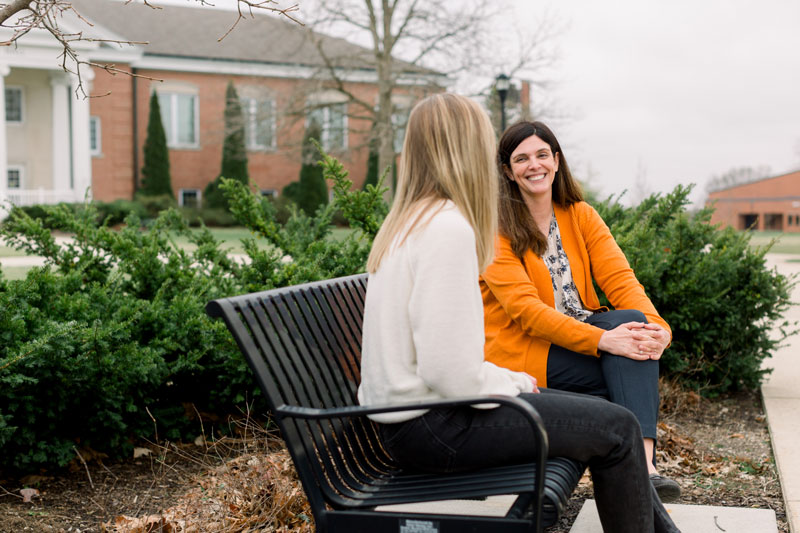 A couple students talking on a bench in front of Ayres Hall