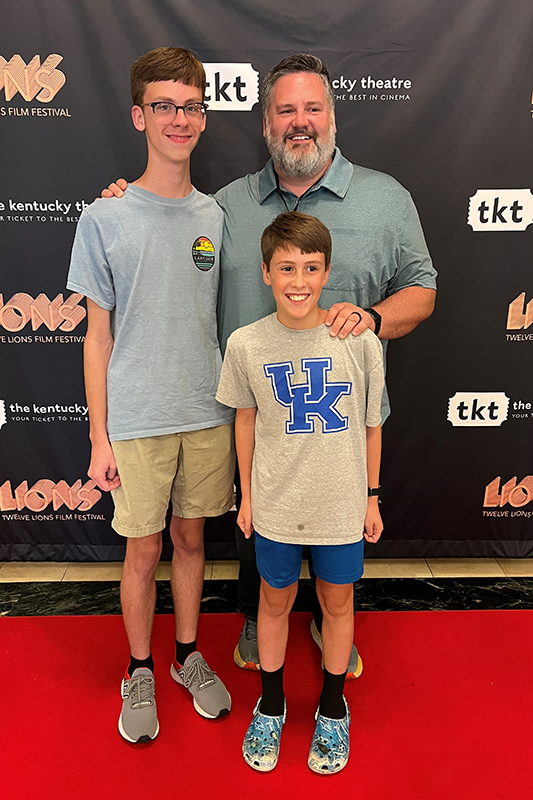 Three people pose on a red carpet in front of a Twelve Lions Film Festival step-and-repeat backdrop.