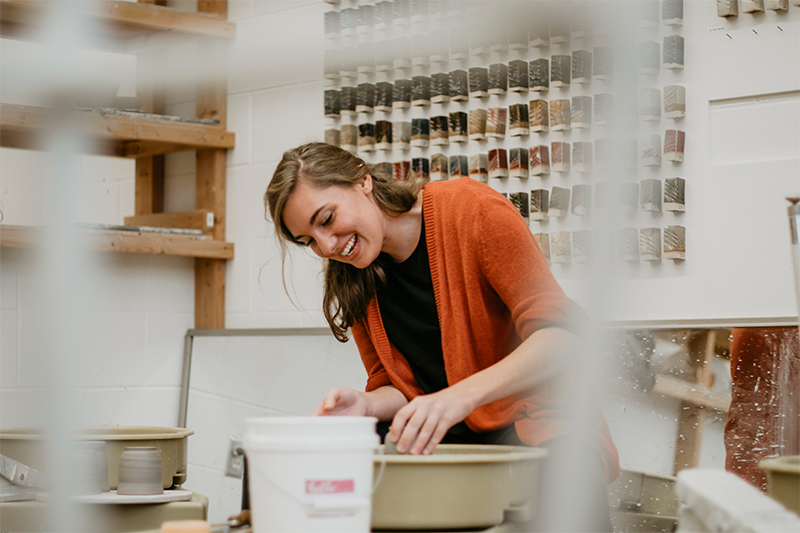 student making pottery and smiling