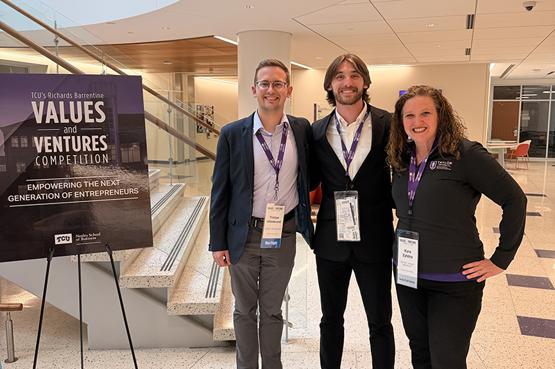 Three conference attendees, including Lextin Willis, wearing lanyards pose in a lobby beside a sign for TCU’s Values and Ventures Competition.