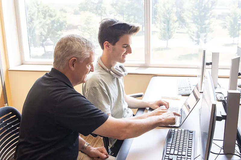 student at computer and professor pointing