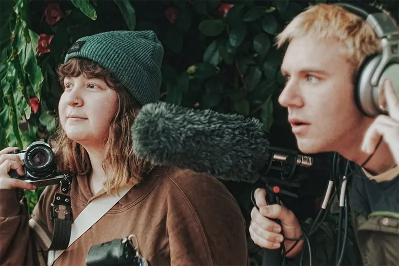 two students, one holds camera and one holds mic