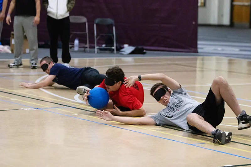 three guys stretch across the court to block the goalball