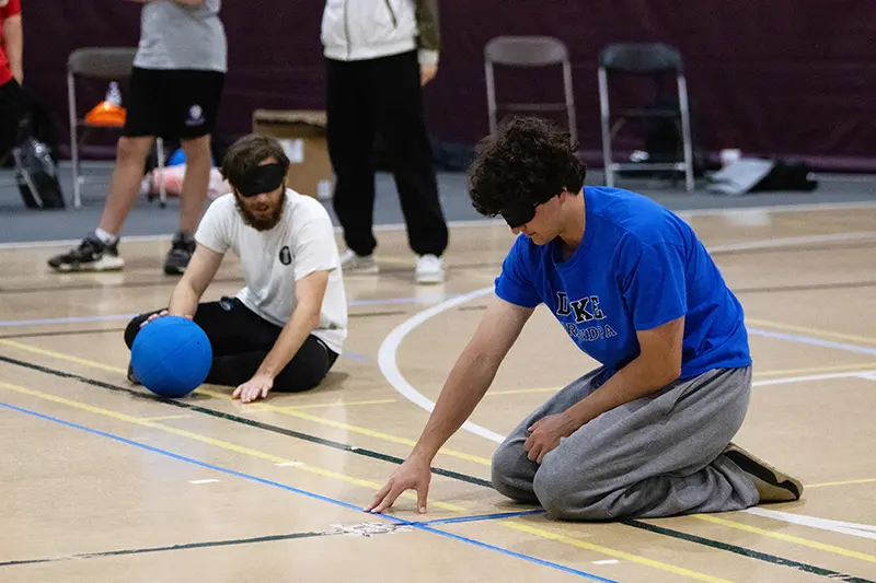 Two students kneel and feel the tape boundary lines on the goalball court