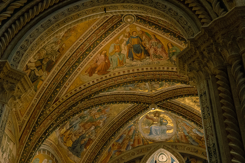 Ornate church vault ceiling with arched frescoes depicting religious figures, framed by decorative stonework and gold accents.