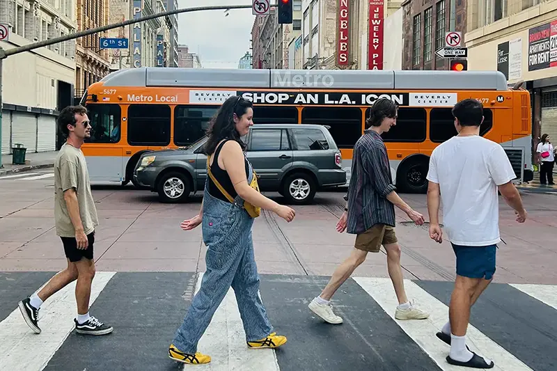 Four students crossing an LA street in front of an orange Metro bus.