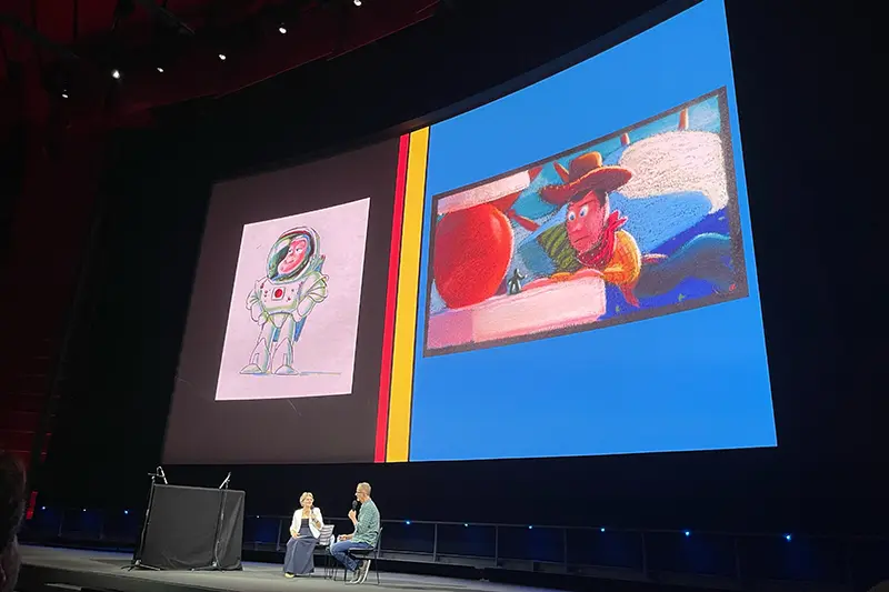 Two people onstage in front of a large screen showing animated character artwork and a film clip.