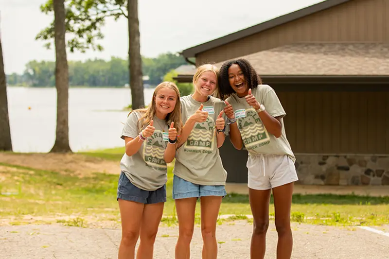 three girl counselors pose with thumbs up outdoors